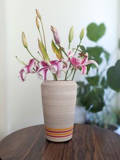 a vase filled with pink flowers on top of a wooden table next to a potted plant