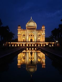 a large building lit up at night with water reflecting in the foreground and palm trees behind it