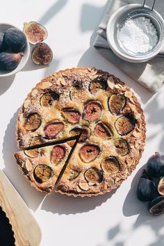 a pie sitting on top of a white table covered in figs and other fruit