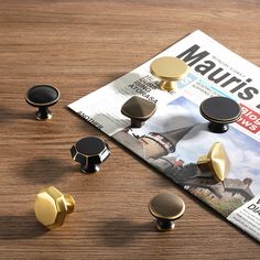 an assortment of metal knobs on top of a wooden table next to a magazine