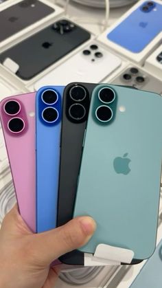 someone holding four different colored iphones in front of some other cell phones on display