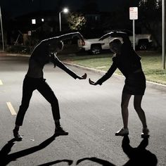 two people holding hands while standing on the side of a road at night with street lights in the background