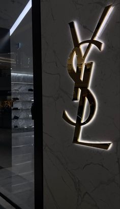 the ysl logo is lit up in front of a wall with marble and gold accents