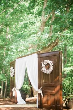 an outdoor ceremony area with white drapes and flowers on the door, surrounded by trees