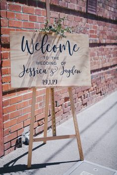 a welcome sign for the bride and groom on a city street with brick wall behind it