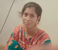 a woman with large hoop earrings on her head sitting in front of a white wall