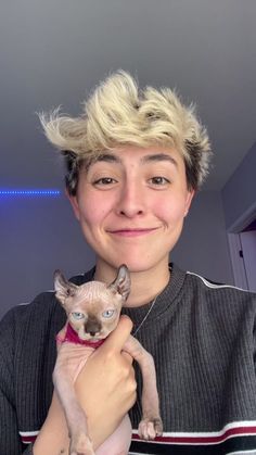 a woman holding a cat in her arms and smiling at the camera while wearing a sweater