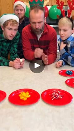 a group of children sitting around a table with red plates on it and one man standing in front of them