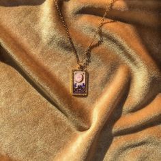 a necklace with an image of a woman in the moon and stars on it sitting on a gold cloth