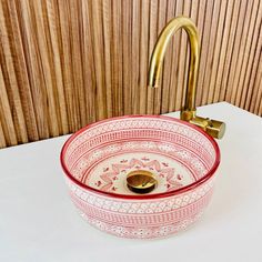 a red and white bowl sink sitting on top of a counter next to a faucet