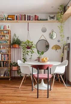 a dining room table with chairs and bookshelves in the background, surrounded by plants