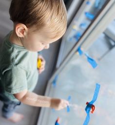 a little boy standing next to a window with blue tape on it's side