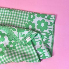 two green and white flowered cloths laying on top of each other in front of a pink background