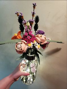 a person holding a vase with flowers in it on a table next to a wall