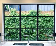 a kitchen sink sitting under a large window next to a counter top with two faucets