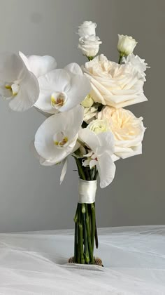 a bouquet of white flowers in a vase on top of a table with a gray background