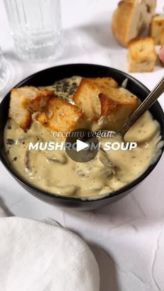 a bowl filled with soup next to bread on top of a white cloth covered table