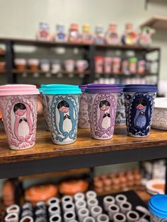 there are many cups on the table in this shop, each with different designs and colors