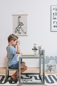 a little boy sitting at a table in front of a wall with pictures on it