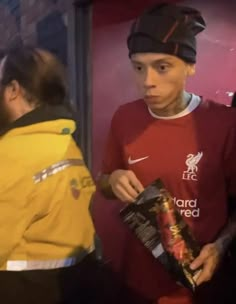 a man in a red shirt holding a bag of food and standing next to another person