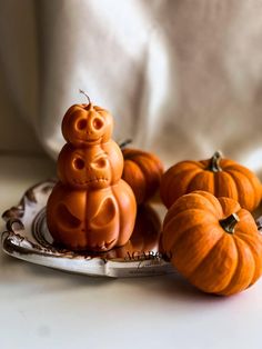 two pumpkins sitting on top of a plate next to some smaller pumpkins with faces carved into them