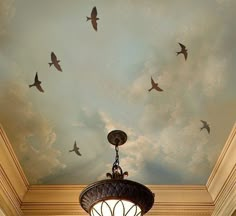 birds are flying in the sky above a chandelier and ceiling painted with clouds