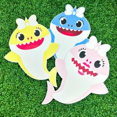 three paper cutouts of shark and baby shark on green grass with fake plants in the background