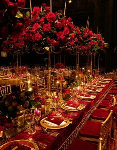 a long table is set with red flowers and gold place settings for an elegant dinner