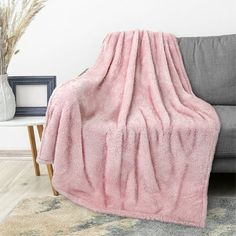 a couch with a purple blanket on top of it next to a vase and plant