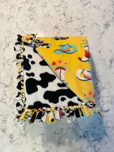 a cow print blanket laying on top of a marble counter next to a yellow and black towel