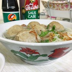 a bowl filled with meat and vegetables next to two bottles of ketchup on a table