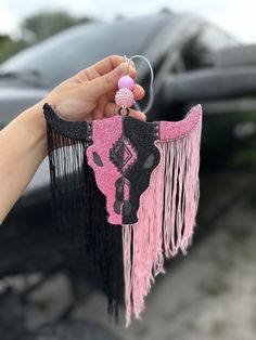 a person holding up a pink and black cow keychain hanging from a car