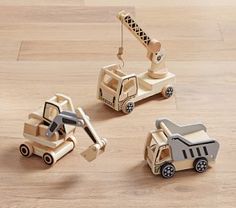 three wooden toy trucks and a crane on a wood floor with light colored floors in the background