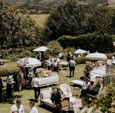 a group of people standing around tables with umbrellas on top of them in the grass