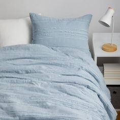 a bed with blue sheets and pillows on top of it next to a night stand