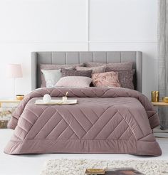 a bed with pink comforter and pillows in a room next to a white rug