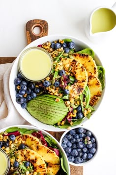 two bowls filled with fruit and vegetables next to glasses of juice