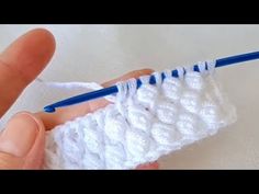 someone crocheting the end of a piece of white yarn with a blue knitting needle