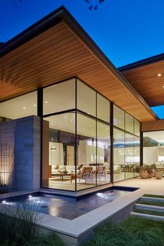 a modern house with glass walls and an outdoor swimming pool at night in the evening