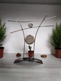 a metal sculpture sitting on top of a table next to potted plants and rocks