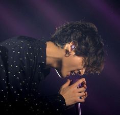 a young man holding a microphone in his right hand and singing into the microphone on stage