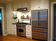 a stainless steel refrigerator and stove in a kitchen with white cabinets, wood flooring and hardwood floors