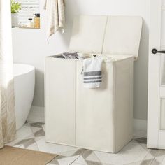 a white laundry hamper sitting on top of a floor next to a bath tub