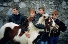 three boys are standing next to a small brown and white horse with long hair on it's back