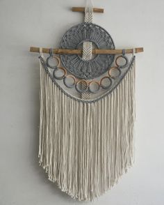 a white wall hanging with fringes and circles on it's sides, along with a wooden stick