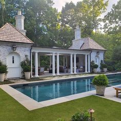 an outdoor pool surrounded by greenery next to a white house with columns and pillars