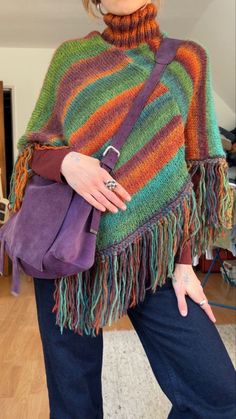 a woman wearing a multicolored ponchle and holding a purple handbag