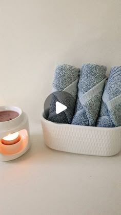 a white bowl filled with blue towels next to a candle