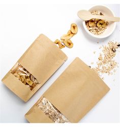 two brown paper bags filled with food next to a bowl of cereal and spoons