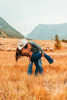 a man and woman kissing in the middle of a field with mountains in the background